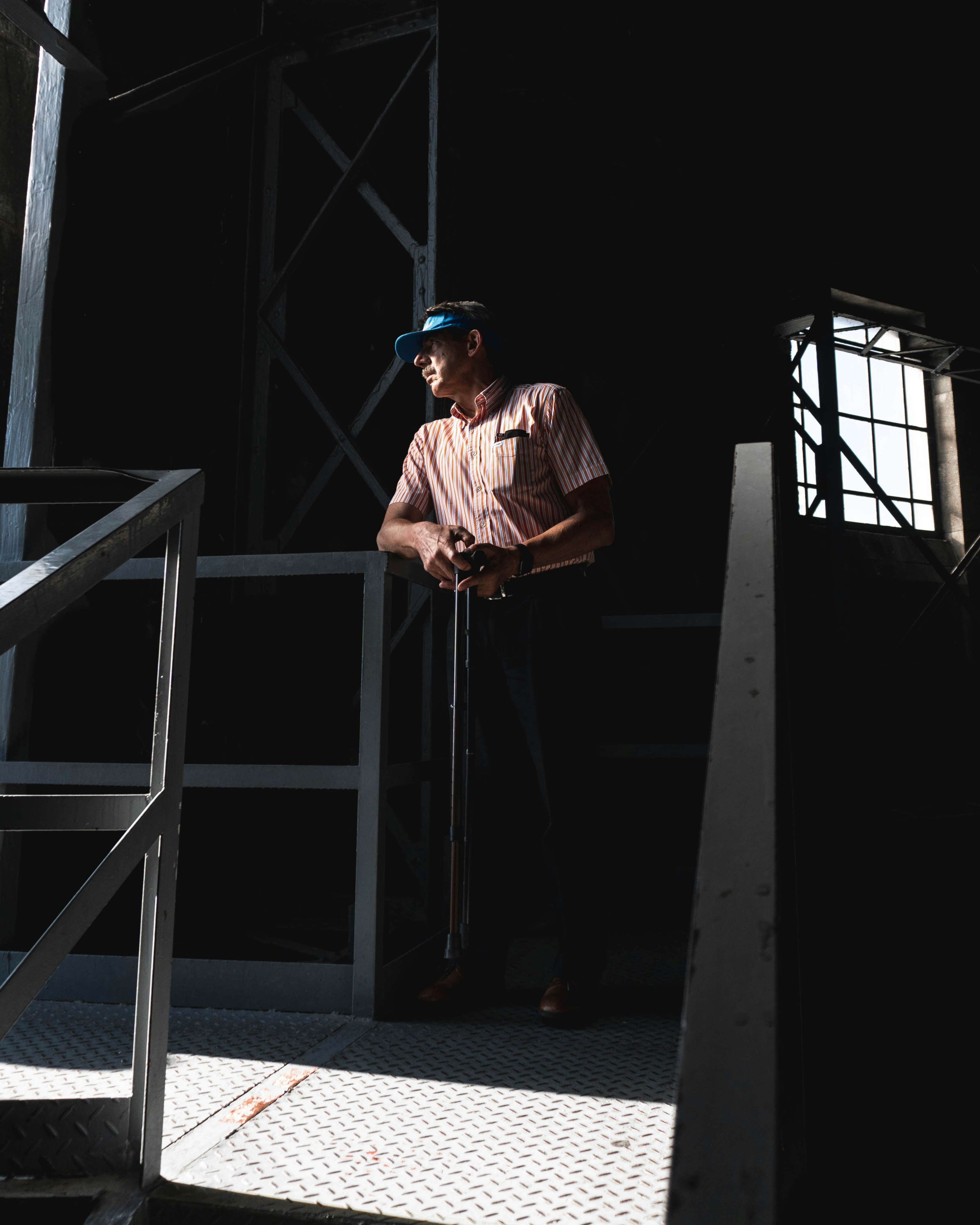 man in orange shirt and blue cap standing beside gray metal railings